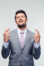 Handsome businessman with fingers crossed over gray background.jpeg